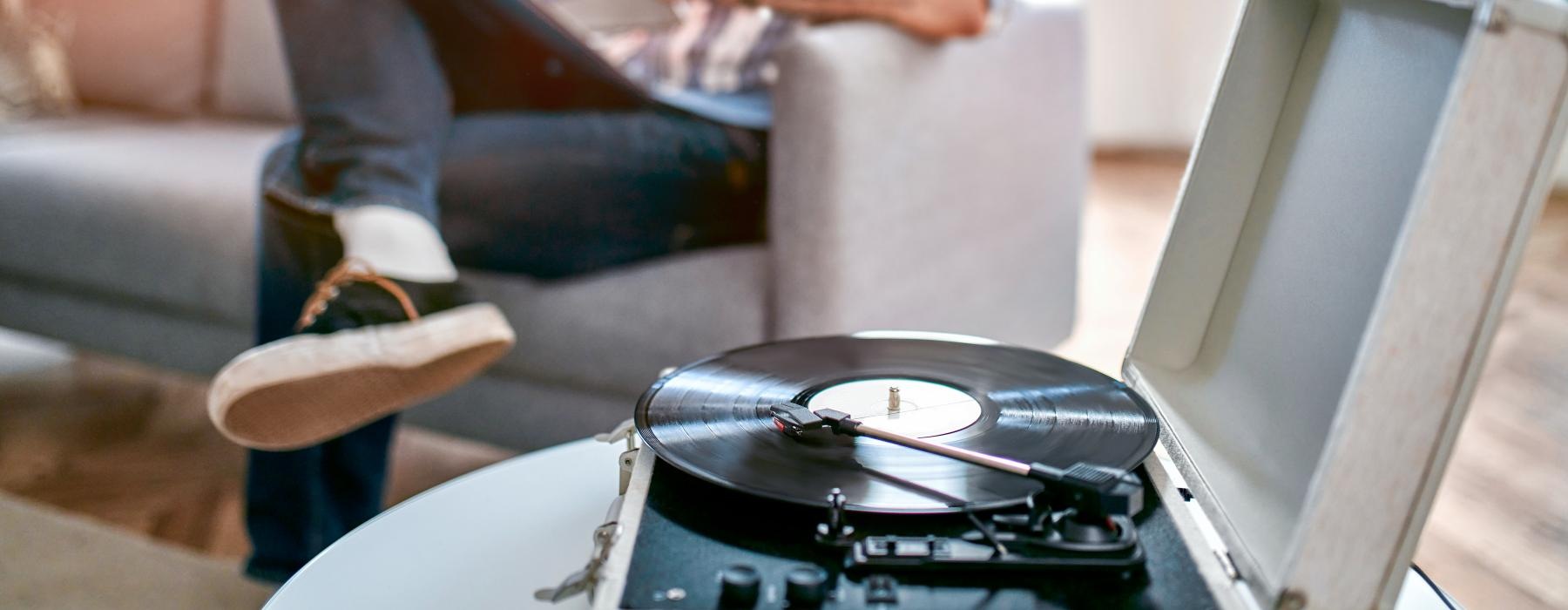 man sits on a chair reading with record player in foreground